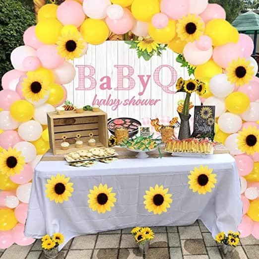 pink and yellow balloon arch with sunflowers over a table decorated for a baby q for girl