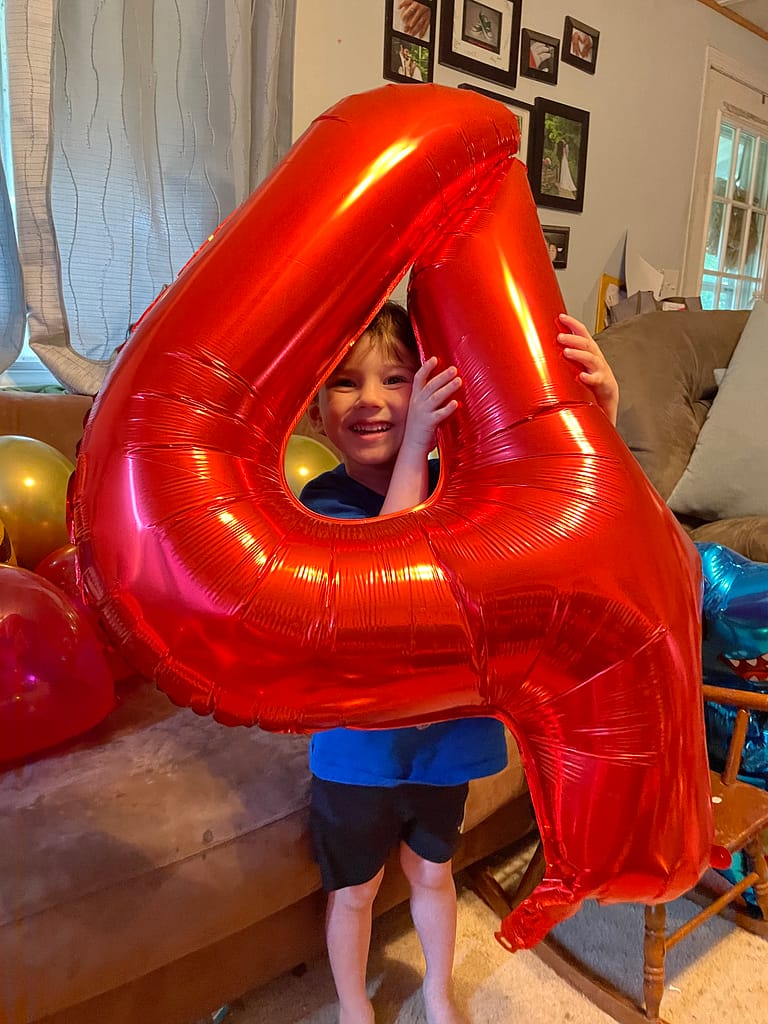 little boy holding a giant red number 4 balloon